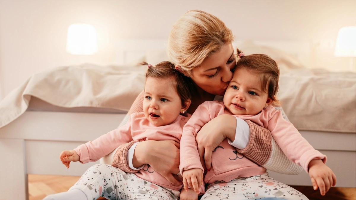 Mom holding her two daughters while kissing one on the cheek 