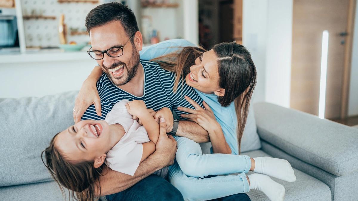 Mom and dad laughing with daughter on couch.