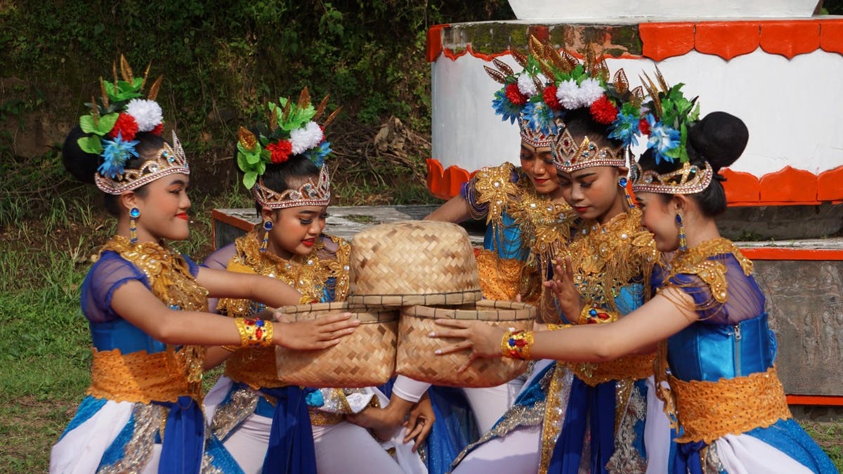 Young women in traditional Acehnese dress are holding baskets and smiling. 